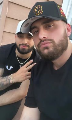 two men sitting next to each other in front of a house