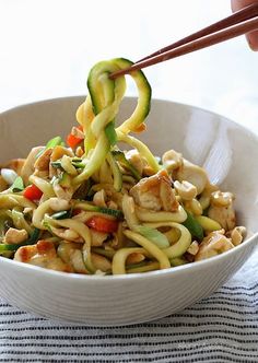 someone is holding chopsticks over a bowl of noodles with chicken and veggies