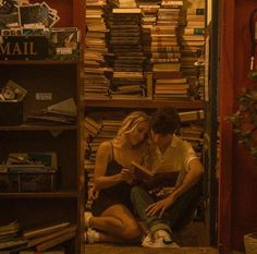 a man and woman sitting on the floor in front of a bookshelf full of books