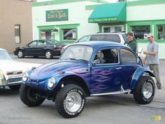 a blue beetle car parked in front of a building with two men standing next to it