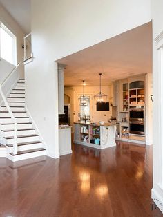 an open kitchen and living room area with hardwood floors, white walls, and stairs