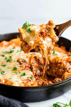 a wooden spoon scooping some lasagna out of a skillet filled with meat and cheese