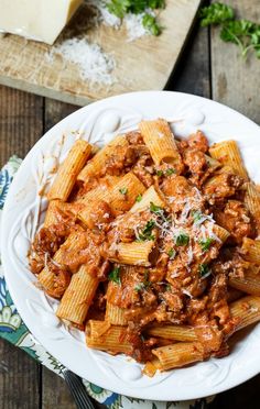 pasta with meat sauce and parmesan cheese on a white plate sitting on a wooden table