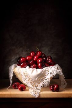 a white cloth bowl filled with cherries on top of a wooden table