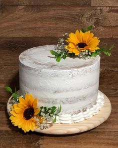 a white cake topped with sunflowers on top of a wooden table