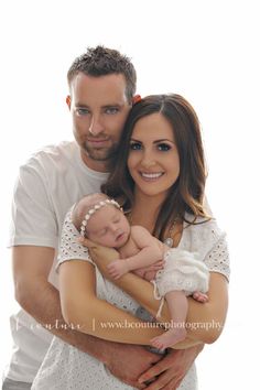 a man and woman holding a baby in their arms, posing for the camera with white background