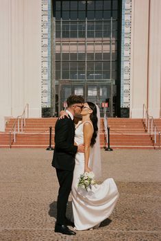 a bride and groom kissing in front of a building