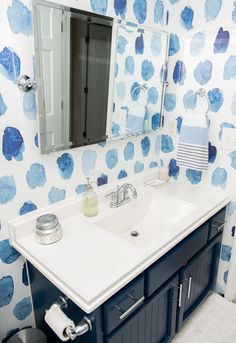 a bathroom sink with blue and white wallpaper on the walls, and a mirror above it