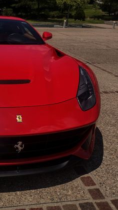 the front end of a red sports car parked in a parking lot next to trees