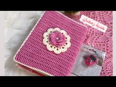 a pink crocheted book with a flower on it and some other items next to it