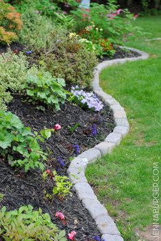 a garden filled with lots of flowers and plants next to a sidewalk in the grass