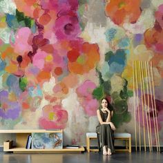 a woman sitting on a bench in front of a colorful wall with flowers painted on it