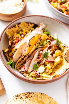 two tacos with meat, vegetables and corn are on the table next to tortillas