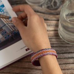 a person is holding an open book and wearing a bracelet on their wrist while sitting at a table