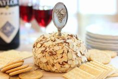 a cheese ball covered in nuts and crackers on top of a table next to wine glasses