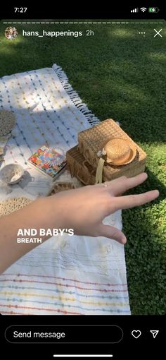 a person's hand on a picnic blanket with bread and other items in the background