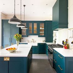 a large kitchen with blue cabinets and white counter tops, along with a bowl of fruit on the island