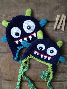 two crocheted hats with monster faces on them, one is green and the other is blue