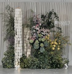 an arrangement of flowers and greenery on display in front of a curtained backdrop