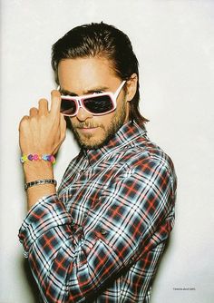 a man with long hair and sunglasses is posing for a photo in front of a white wall