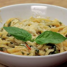 a white bowl filled with pasta covered in sauce and cheese topped with green leafy garnish