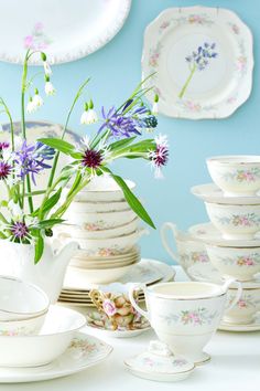 a table topped with lots of white dishes and cups filled with flowers in vases