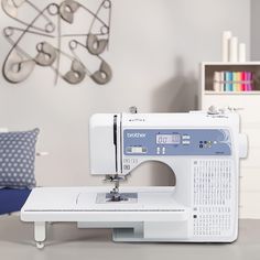 a white sewing machine sitting on top of a table next to a blue and white pillow