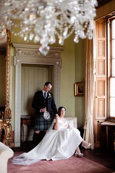 a bride and groom pose for a wedding photo in front of a large mirror with chandelier hanging from the ceiling