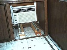 an air conditioner sitting in the corner of a room with tile flooring and wooden cabinets