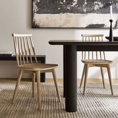 two wooden chairs sitting at a table in front of a painting