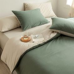 a bed with green and white sheets in a bedroom next to a lamp on a nightstand