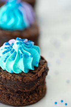 three chocolate cupcakes with blue frosting and sprinkles on them