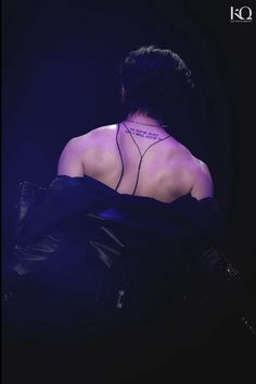 the back of a woman with tattoos on her neck and chest, sitting in a dark room