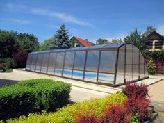 there is a glass house in the middle of some plants and bushes on the side of the road