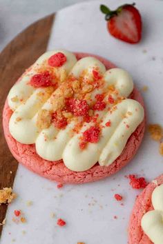 two cookies with white frosting and red sprinkles sit on a cutting board