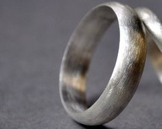 two wedding bands made out of silver and yellow gold, on a gray surface with one ring in the middle