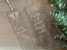 two glass bookmarks with writing on them sitting next to some leaves and flowers in the background