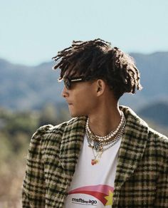 a young man with dreadlocks wearing a t - shirt and plaid blazer