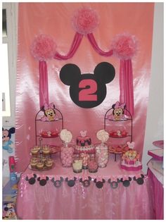 a table topped with lots of desserts and candy covered in minnie mouse decorations on top of a pink backdrop