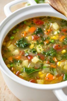 a white bowl filled with vegetable soup next to a wooden spoon