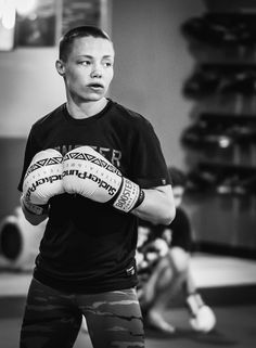 black and white photograph of a man wearing boxing gloves in a gym with one hand on his hip