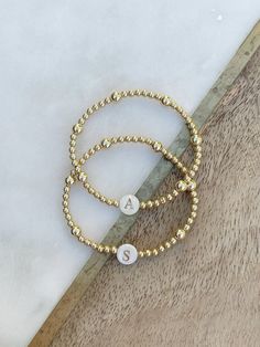 This listing is for ONE beautiful gold filled beaded bracelet with 3mm and 5mm gold filled beads, and a gorgeous shell bead w/gold letter of your choice.  SO beautiful to wear on its own or perfect to layer with your bracelet stack.  Versatile and classic- a treat for yourself or makes the best gift for your loved ones! Please note- the distribution of the 3mm and 5mm beads may be different than pictured, depending on size, but it will look very similar to the samples.   If unsure of sizing, mea Gold Beaded Bracelets With 14k Gold-filled Round Beads, Gold Beaded Bracelets With 14k Gold Filled Round Beads, Elegant Personalized Gold Beaded Bracelets, Gold Hypoallergenic Name Bracelet With Round Beads, Personalized Gold Stretch Bracelet, Personalized Gold Round Stretch Bracelet, Gold Stretch Bracelet With Letter Beads, Gold Beaded Bracelet With Tiny 14k Gold Filled Beads, Gold Hand-strung Stretch Bracelet In 14k Gold-filled