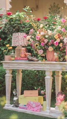 a table topped with lots of flowers and books next to a lamp on top of a wooden table