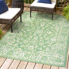 an outdoor area with two chairs and a rug on the ground, in front of a wooden deck