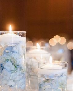 two clear vases filled with white flowers and lit candles