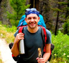 a man with a backpack and water bottle walking on a trail