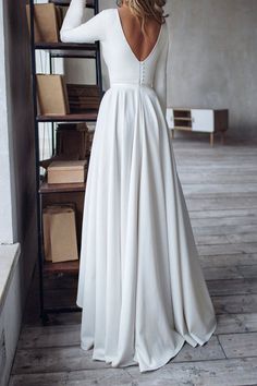 a woman standing in front of a book shelf wearing a white dress with long sleeves