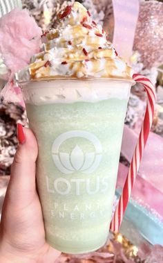 a hand holding up a green drink with whipped cream and candy canes on top