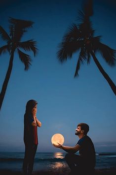 a man holding a light up in front of a woman on the beach with palm trees