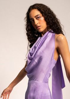 The lavender drape jumpsuit features a flattering pleated cowl neckline that drapes gracefully, adding a touch of sophistication to the outfit. Tied up with a delicate neck tie, the back showcases an elegant yet subtly provocative look. The luxurious modal satin fabric not only ensures a lustrous appearance but also offers a comfortable and flattering fit, making this jumpsuit a perfect choice for those seeking a blend of style and comfort. Whether it's a special evening event or a fashionable c Elegant Spring Jumpsuits And Rompers With Back Opening, Elegant Evening Jumpsuit With Tie Back, Elegant Purple Jumpsuits And Rompers For Party, Evening Jumpsuits And Rompers With Tie Back, Elegant Sleeveless Purple Jumpsuits And Rompers, Elegant Purple Party Jumpsuits And Rompers, Elegant Purple Jumpsuit For Party, Chic Lavender Jumpsuits And Rompers For Summer, Drape Jumpsuit